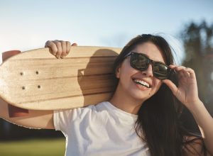 Emotions, youth and city skateboarding concept. Close-up cheerful happy skater girl hold wooden penny board on shoulder, laughing carefree touching sunglasses, enjoy sunny summer afternoon ride.