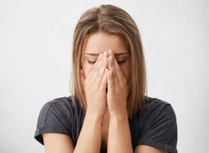 Young female dressed casually covering face with both hands, feeling nervous or ashamed, not looking at camera, hiding herself. Human facial expressions, emotions, feelings, reaction and attitude