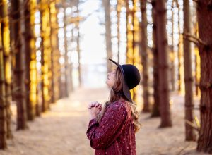 A selective focus shot of a beautiful young lady praying in a forest
