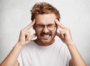 Headshot of stressful emotionl bearded male has terrible headache, expresses tiredness, keeps fingers on temples, feels frustration and migraine, isolated over white background. Negative feelings